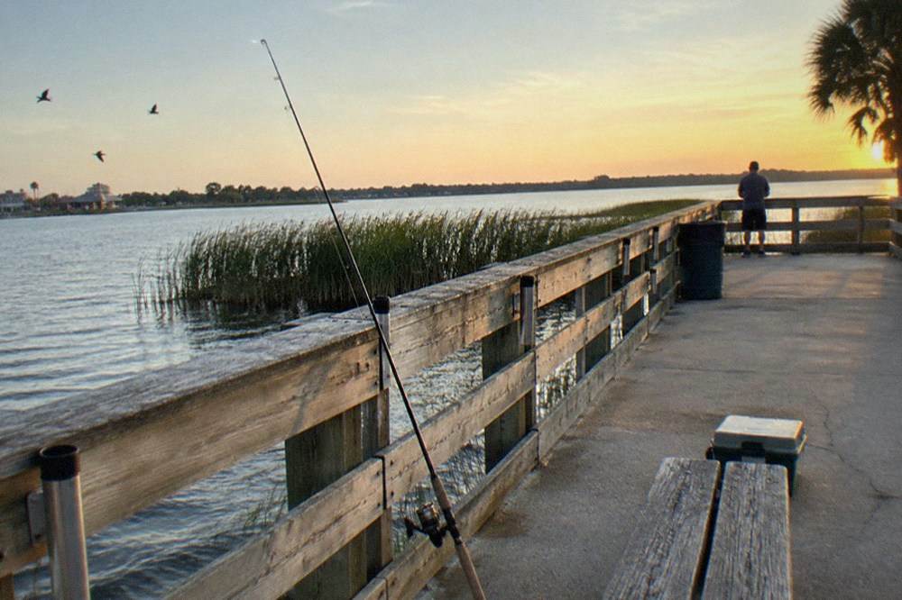 Fishing pier over calm Florida water with rod holders and an empty bench