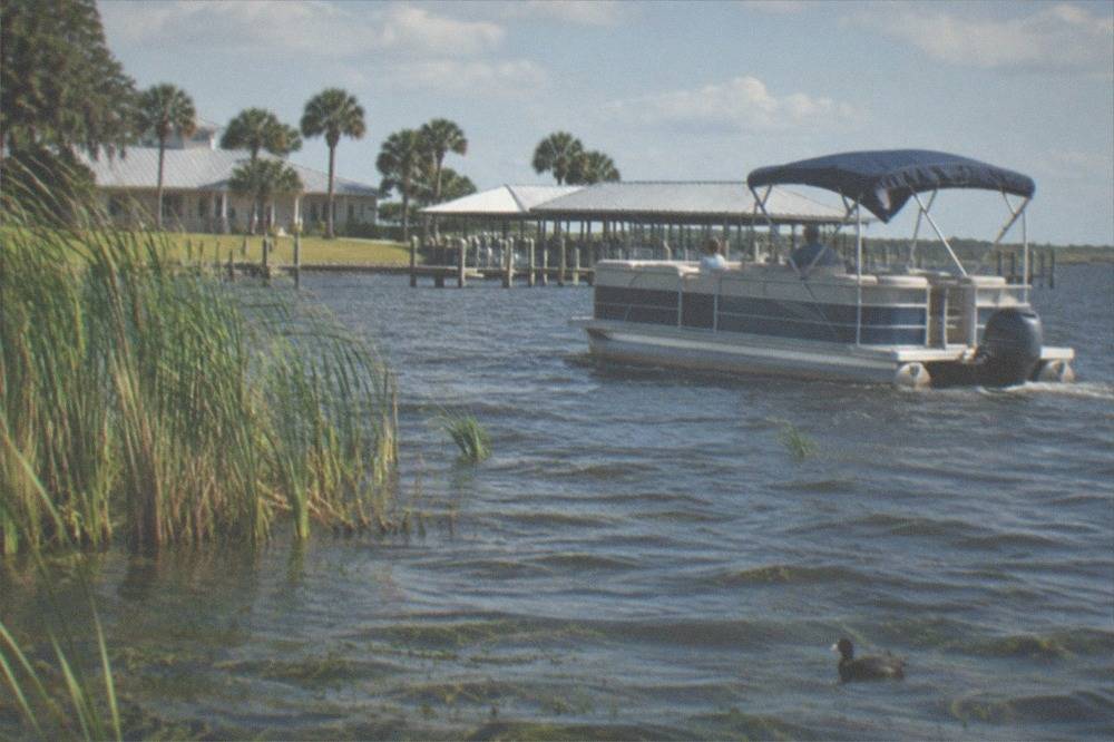 Pontoon boat drifting on a wide Florida bass lake with reeds along the shore