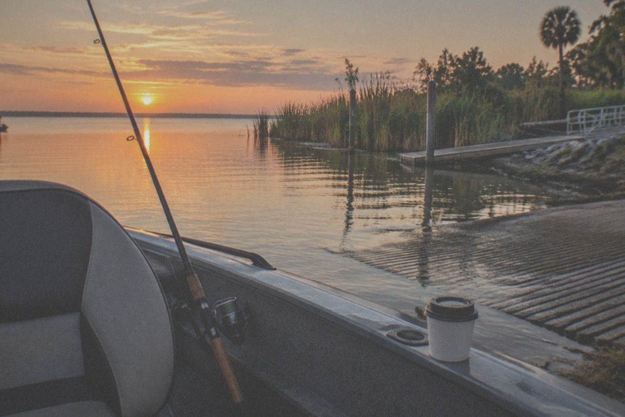Calm Florida lake at sunrise with a fishing rod resting against a boat seat