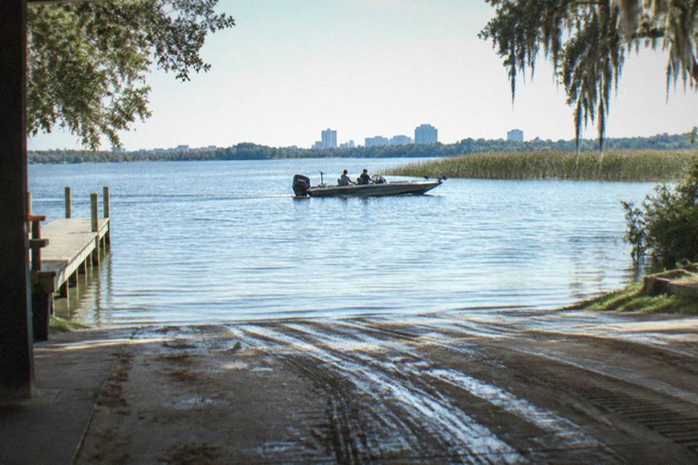 A private bass boat cruising across open water toward a line of cattails on a Central Florida lake