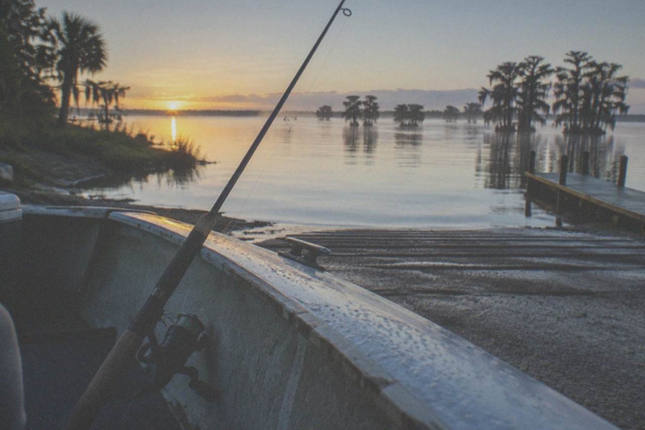 Calm lake water at first light with a fishing rod resting against the gunwale of a small boat
