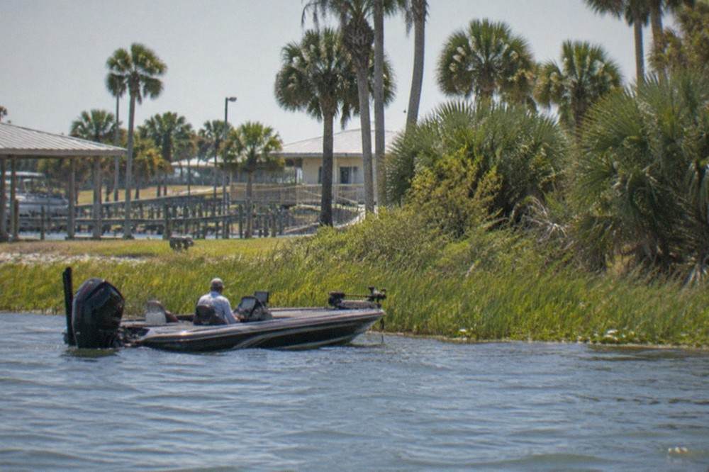 Bass boat drifting along a grassy shoreline on a large shallow Florida lake at midday