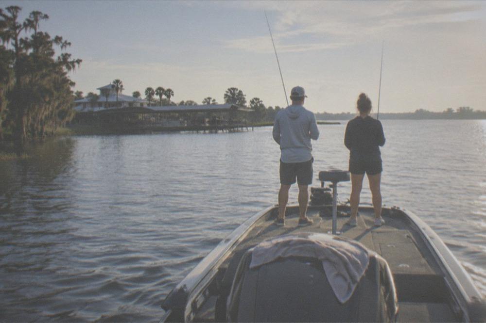 Guide and guest at the back of a bass boat with rods up as the boat idles across open water