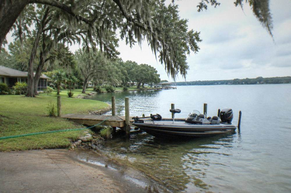 Bass boat at a residential lake shoreline with clear water and trees