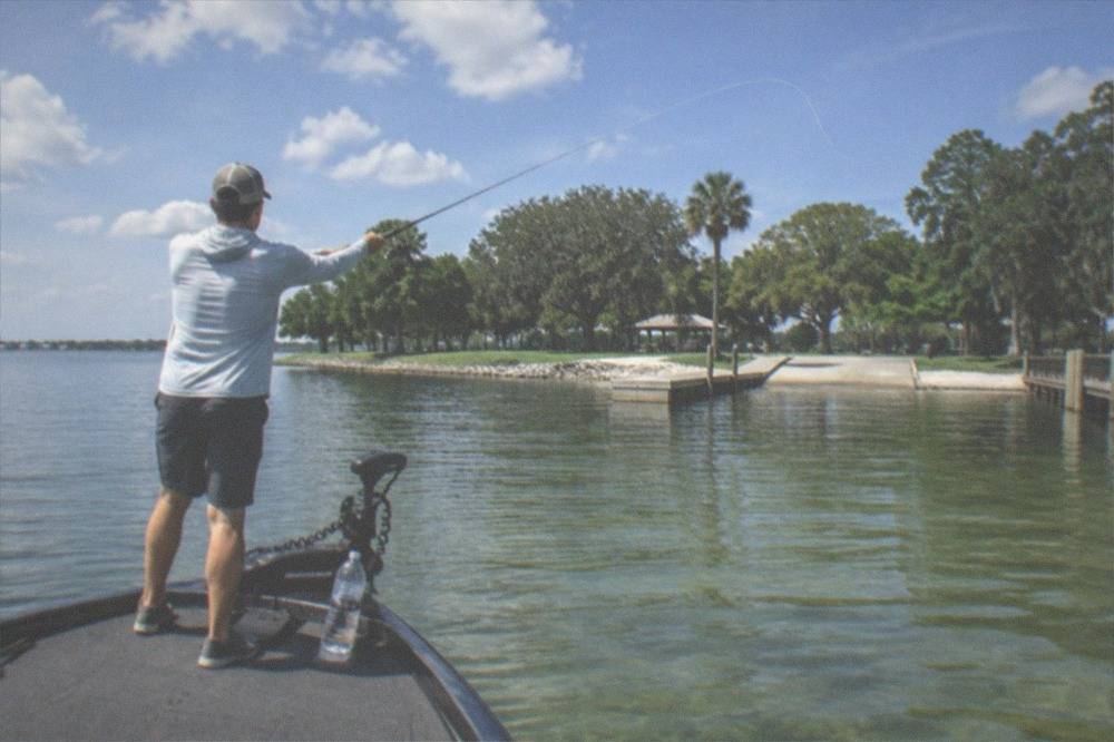 Angler casting a fishing rod from the bow of a boat on open lake water