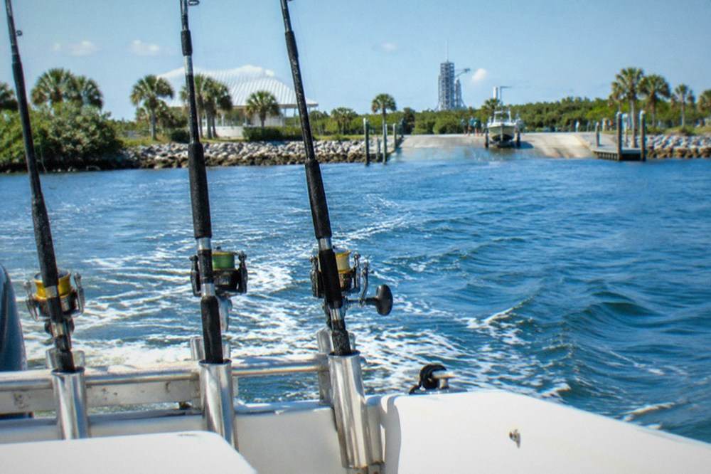 Rods in holders along the stern of a charter boat with blue open ocean beyond the rail.