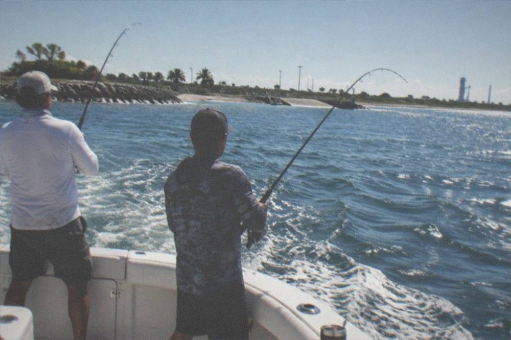 Anglers fishing from the stern of a private charter boat with rods bent over blue offshore water.