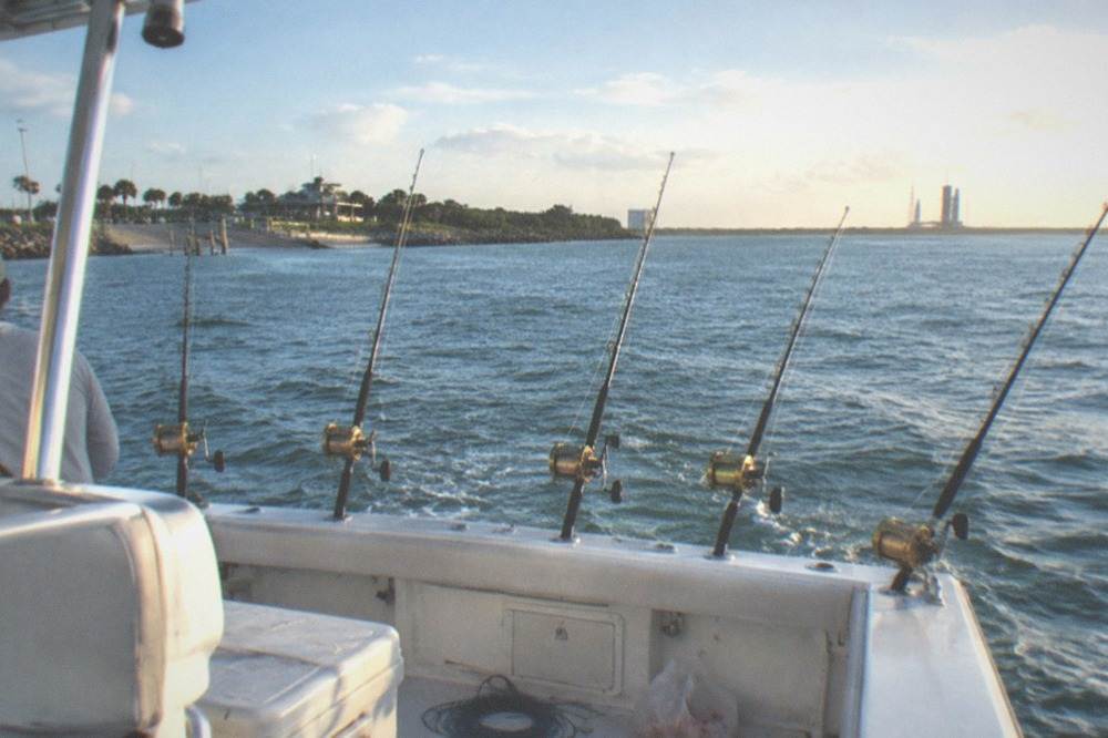 A charter boat trolling offshore with multiple rods spread out over calm blue water.