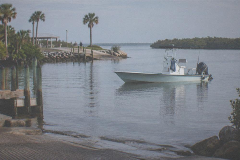 A shallow-draft charter boat drifting over calm lagoon water with mangrove shoreline in the distance.
