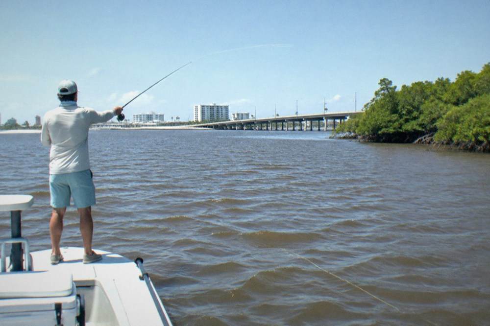 An angler casting from the deck of a flats skiff on open lagoon water