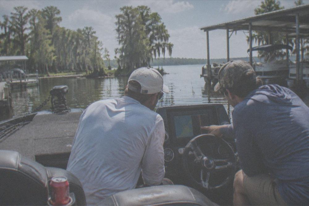 A guide and guest reviewing a map at the console of a bass boat