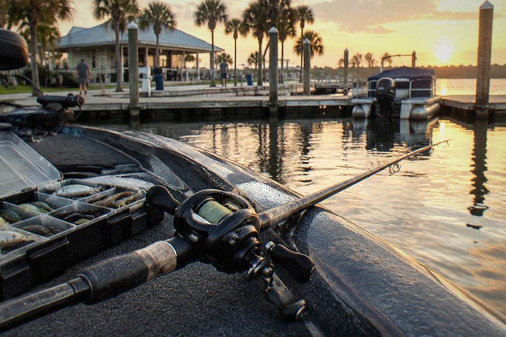 A baitcasting rod resting on the gunwale of a bass boat beside a tackle box