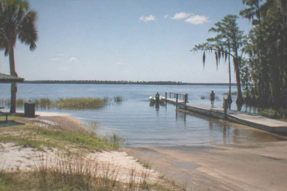 A wide view of a glassy Florida lake with sparse reed beds and open water at midday