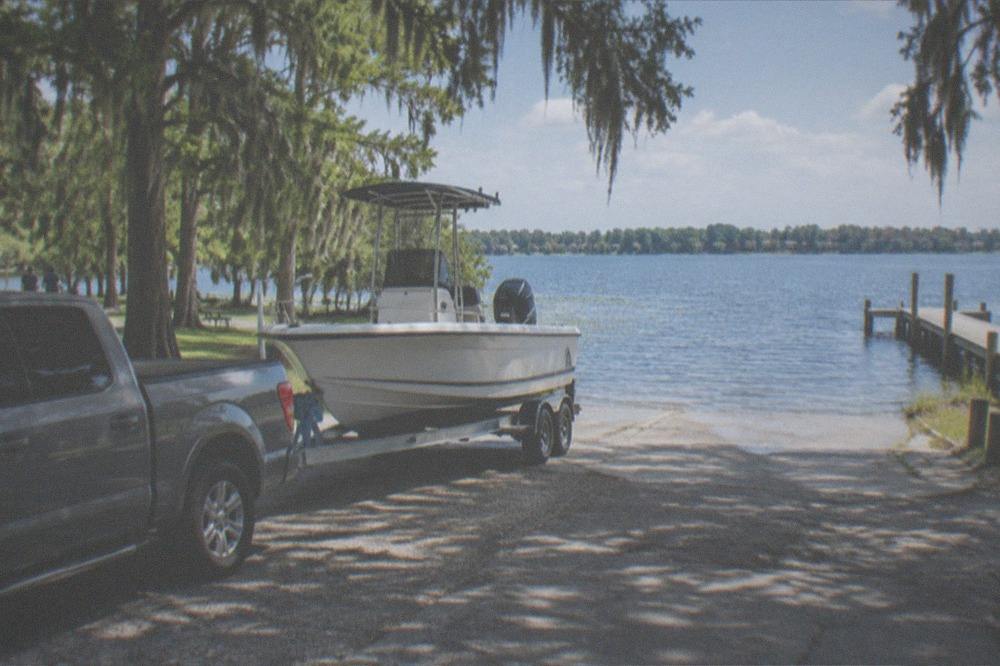 A pickup truck with a boat trailer parked at a lake ramp under a bright sky