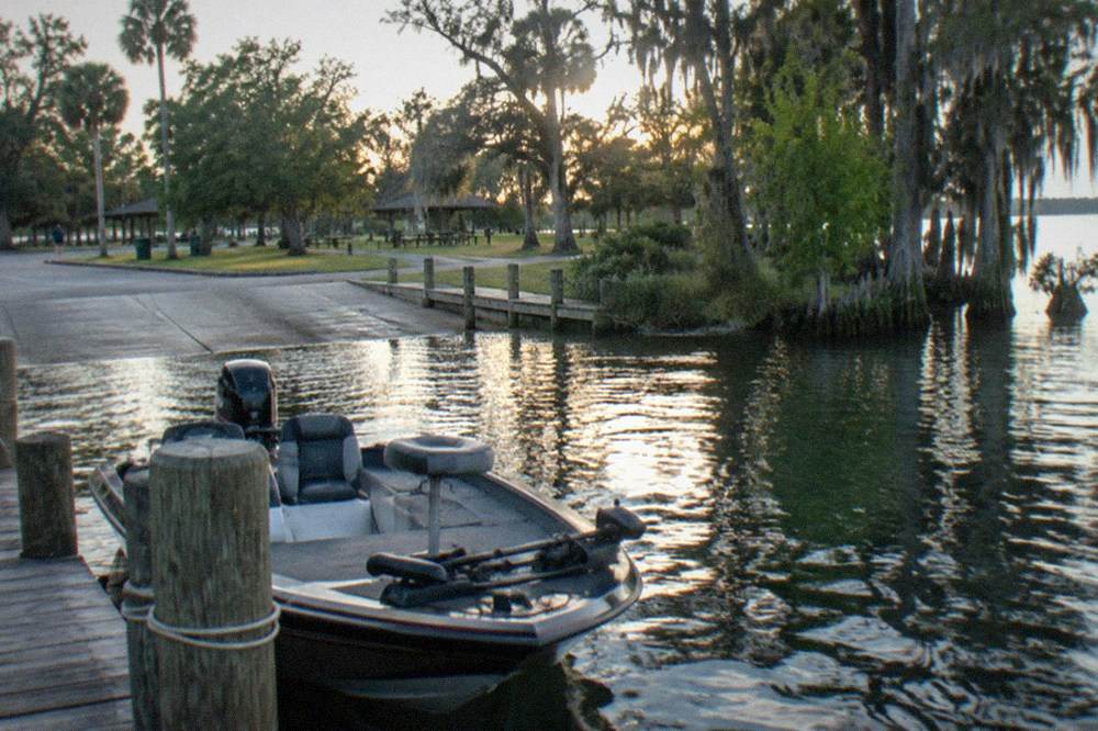 A fishing boat tied at a wooden dock on a Florida lake with cypress trees along the shore