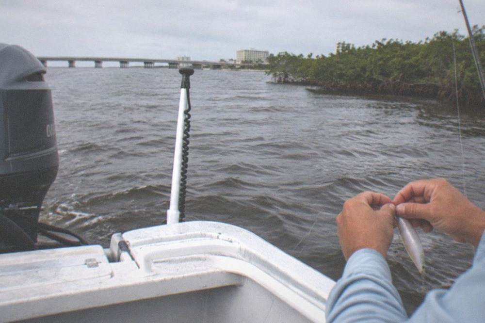 A guide's hands tying a fishing lure at the back of a boat near the water