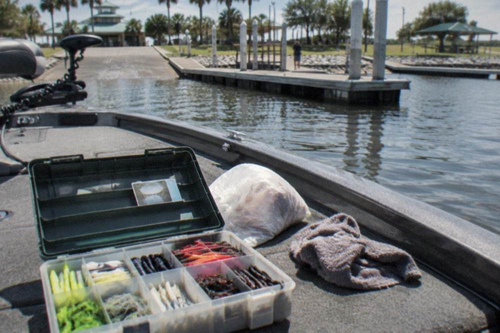 A tackle box open on a boat deck with organized lures and a fishing licence card tucked inside