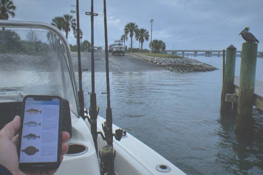 A smartphone displaying a fishing regulations webpage held above a boat console