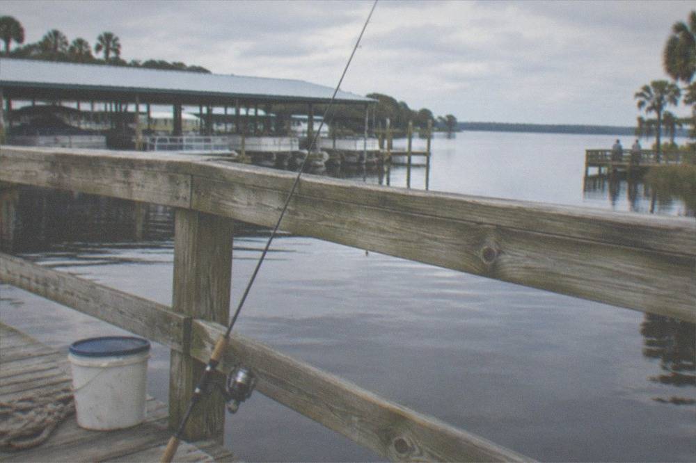 Fishing rod resting against a wooden dock above calm lake water