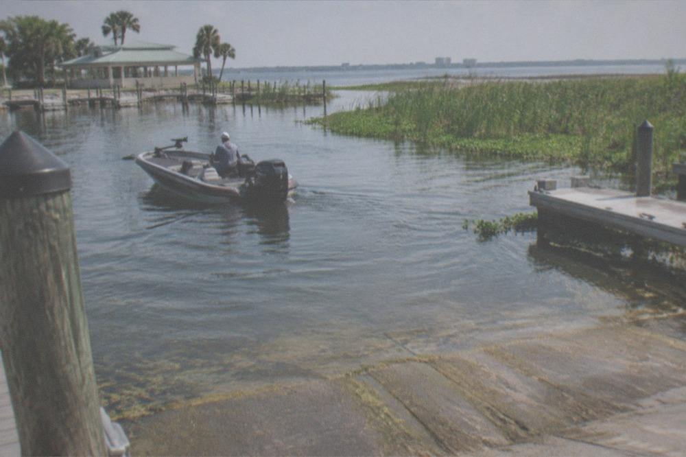 Charter captain at the tiller of a bass boat scanning a flat Florida lake shoreline