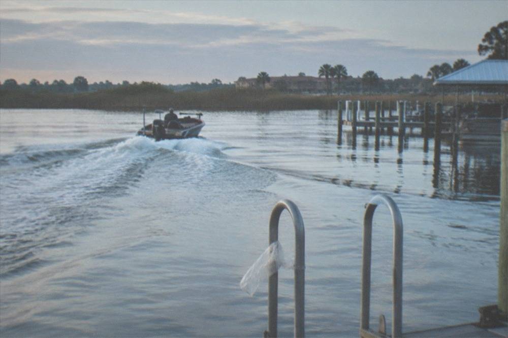 Early morning light over a calm lake with a bass boat wake cutting across open water