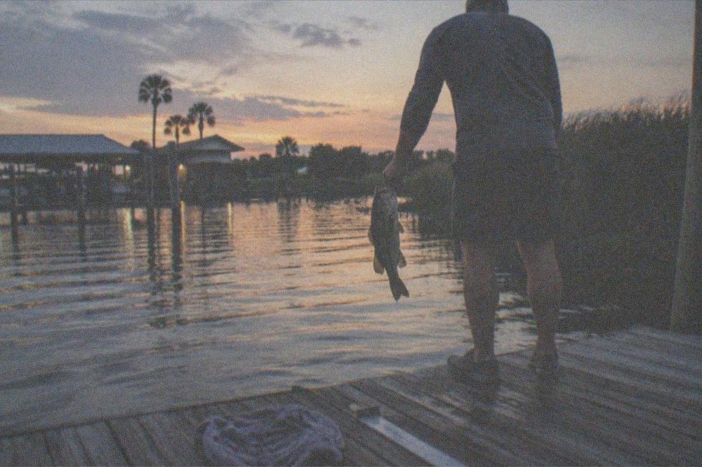 Angler holding a largemouth bass over a lake with reeds behind