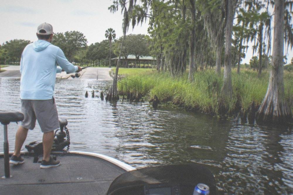 An angler casting toward a grassy lake shoreline from the deck of a small charter boat