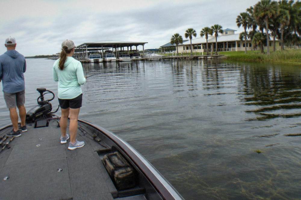 Two anglers casting from the front deck of a bass boat on a calm lake