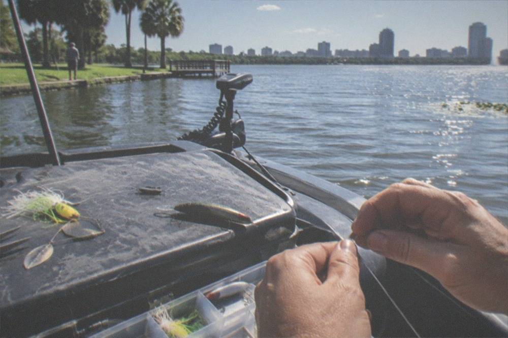 Close view of a tackle box with lures and a hand tying a fishing knot