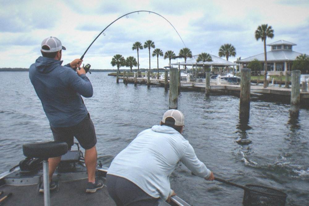 Angler reeling in a bent rod while a guide reaches with a landing net
