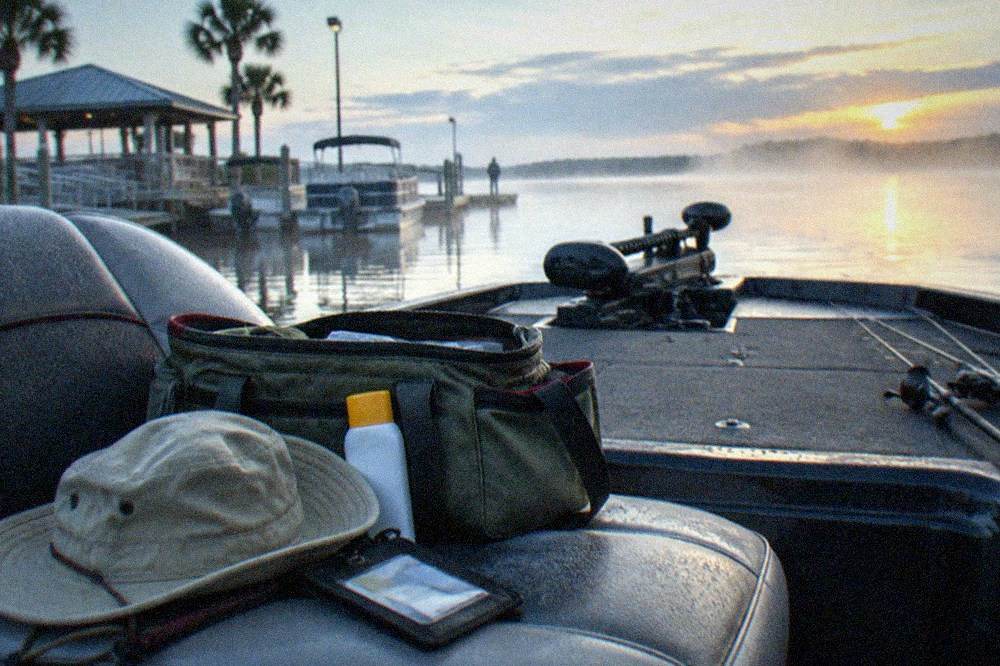 Angler's bag with sunscreen, hat and licence holder resting on the seat of a bass boat at a marina