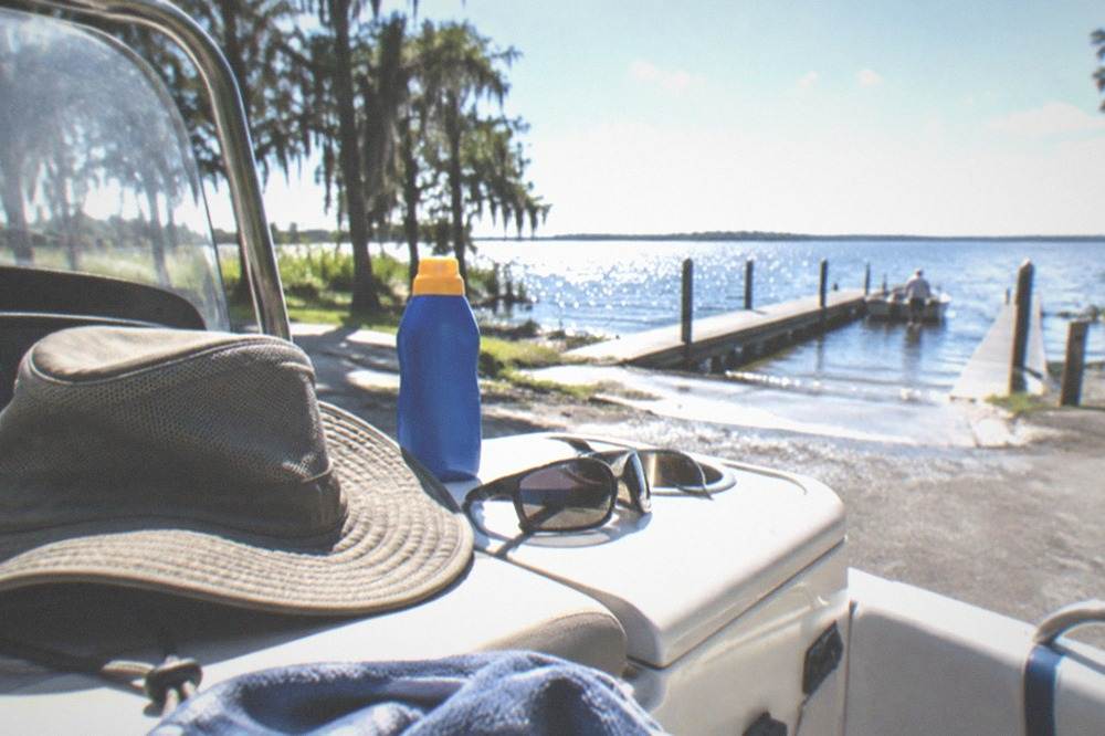 Wide-brim hat, sunscreen bottle and polarized sunglasses on a boat console in bright sunlight