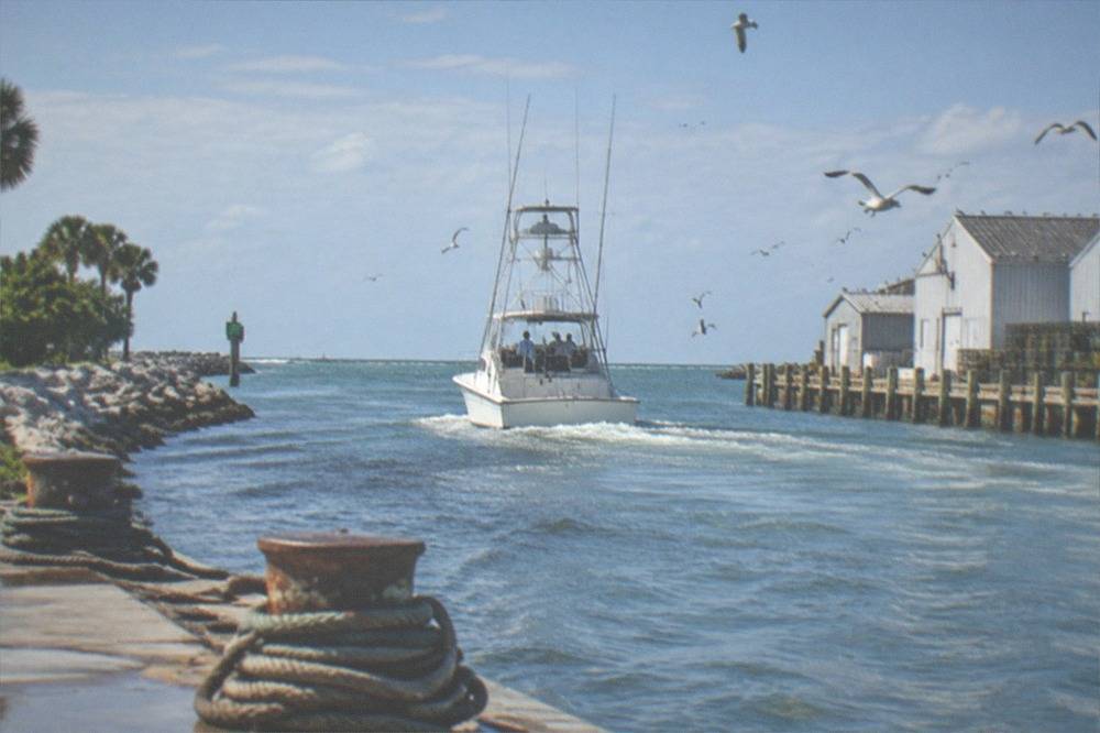Offshore sportfishing boat heading out through a port channel toward open Atlantic water