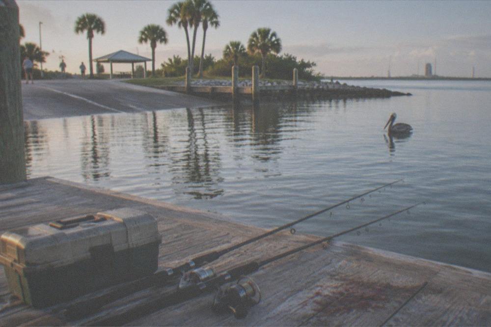 Fishing tackle box and rods laid out on a dock beside calm morning water